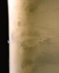 NASA's Mars Global Surveyor shows clouds common in late spring over martian terrain located southwest of the Arsia Mons volcano. Arsia Mons is the dark, oval feature near the limb.