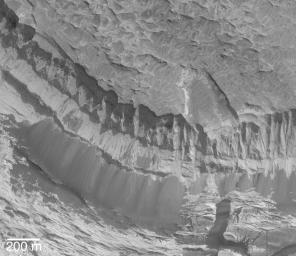NASA's Mars Global Surveyor shows a vista of sedimentary rocks outcropping on a slope in Aram Chaos on Mars. Dark piles of coarse talus have come down the slopes as these materials continue to erode over time.