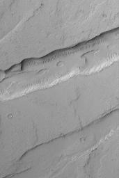NASA's Mars Global Surveyor shows troughs and a pit chain (on the floor of the deeper trough) located immediately northeast of the giant Tharsis volcano, Arsia Mons on Mars.