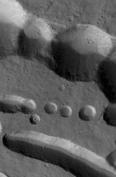 NASA's Mars Global Surveyor shows collapse pits on the northern flank of the giant Tharsis shield volcano, Ascraeus Mons on Mars. Large, dark boulders occur on the floors of some of the pits.