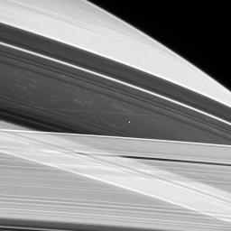 Saturn's shepherd moon Prometheus hovers between the A and F rings as if suspended on an invisible thread, while bright clouds drift in Saturn's atmosphere approximately 130,000 kilometers beyond. This image was captured by NASA's Cassini spacecraft.