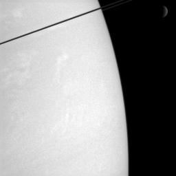 Whiffs of cloud dance in Saturn's atmosphere, while the dim crescent of Rhea hangs in the distance. The dark ringplane cuts a diagonal across the top left corner of this view from NASA's Cassini spacecraft. 
