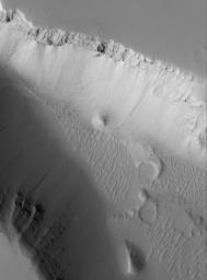 NASA's Mars Global Surveyor shows a high resolution view of the floor and walls of a trough located west of the Elysium Mons volcano on Mars. The trough cuts through layered and dust-mantled rock.