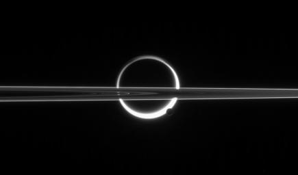 Saturn's rings cut across an eerie scene that is ruled by Titan's luminous crescent and globe-encircling haze, broken by the small moon Enceladus, whose icy jets are dimly visible at its south pole this image taken by NASA's Cassini spacecraft.