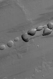 NASA's Mars Global Surveyor shows a portion of a chain of pits on a lava- and dust-covered plain northwest of Tharsis Tholus, one of the many volcanic constructs in the Tharsis region of Mars.