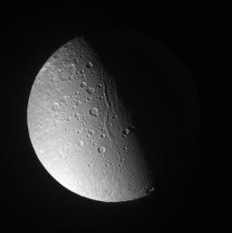 Canyons and mountain peaks snake along the terminator on the crater-covered, icy moon Dione. A line of mountain ridges above center casts shadows toward the east as seen by NASA's Cassini spacecraft.