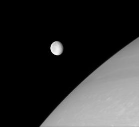 Rhea is frozen in this image from NASA's Cassini spacecraft, captured just before it glided in front of Saturn's northern hemisphere. The wispy streaks on Rhea's trailing side are partly visible in the west.