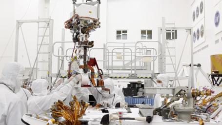 In the clean room at NASA's Jet Propulsion Laboratory, engineers gather around the base of Curiosity's 'neck' (the Mast) as they slowly lower it into place for attachment to the rover's 'body' (the Wet Electronics Box, or 'WEB').
