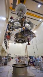 Technicians transfer NASA's Juno spacecraft from its rotation fixture to the base of its shipping container in preparation for a move to environmental testing facilities. Juno's main engine, its cover closed, is visible on the spacecraft's underside.