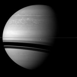 Saturn's moon Tethys orbits in front of the wide shadows cast by the rings onto the planet for this view from NASA's Cassini spacecraft. Tethys appears just below the rings near the center of the image.