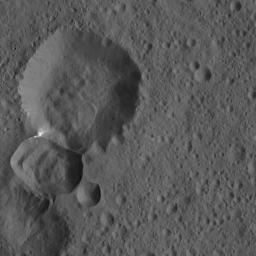 Two adjoining craters on Ceres are featured in this image from NASA's Dawn spacecraft. A lobe-shaped feature is prominent in the larger crater's interior. Bright material is visible at the intersection of the two craters.