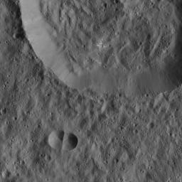 This image from NASA's Dawn spacecraft of Ceres shows a small, double-impact crater (at bottom) near a larger crater. The larger structure has a crater floor with roughly the same crater density.