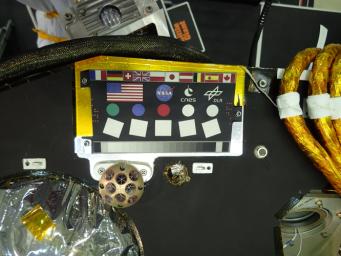 A camera calibration target sits on the deck of the NASA's InSight lander, adorned with the flags of different nations participating in the mission.