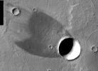 This image, part of an images as art series from NASA's 2001 Mars Odyssey released on Feb 24, 2004 shows that winds blowing over a crater's rim have scoured the ground behind the crater free of light-colored dust, exposing a relatively bare lava flow.