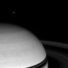 With nearby Saturn looming large, NASA's Cassini spacecraft spies the bright distant moon Tethys in the icy blackness beyond.
