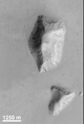 NASA's Mars Global Surveyor shows two buttes in the Elysium Basin on Mars. Exhibited are many small dark streaks on their slopes. Each streak is the result of mass-movement (landslides). Darker streaks appear to be younger than the brighter ones. 