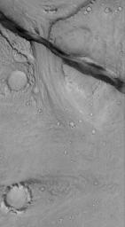 NASA's Mars Global Surveyor shows a landscape in the eastern Cerberus region on Mars scoured by catastrophic floods, and later cut by a deep, dark-walled trough. The trough is radial to the Elysium volcanic region, and formed along faults in the bedrock.
