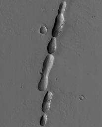 NASA's Mars Global Surveyor shows a chain of pits associated with dust-covered lava flows in northern Tharsis on Mars. The pits formed along a fault; some of the flows may have erupted along this same fault.