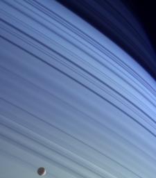 Mimas drifts along in its orbit against the azure backdrop of Saturn's northern latitudes in this true color view. The long, dark lines on the atmosphere are shadows cast by the planet's rings.
