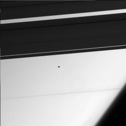 The 'flying saucer' in this image from NASA's Cassini spacecraft is the small moon Atlas (20 kilometers, 12 miles across), whose shadowy profile reveals its flattened shape.