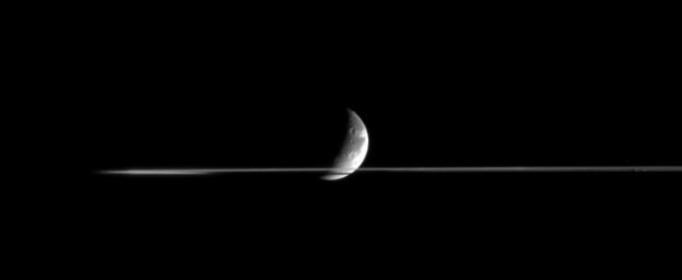 Dione is partly occulted by Saturn's rings in this nearly edge-on view, taken from less than a tenth of a degree above the ringplane. The side of the rings nearer to NASA's Cassini spacecraft was masked by Saturn's shadow at the time and appears dark.