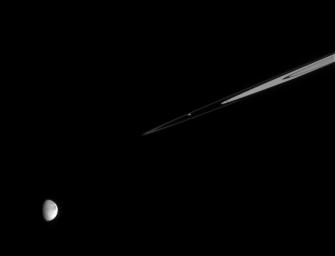 Saturn's ring moon Prometheus continues its work shaping the delicate F ring as Dione looks on. The image was taken in visible light with NASA's Cassini spacecraft's narrow-angle camera on Dec. 20, 2005.