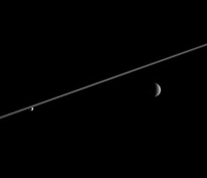 Rhea and Enceladus hover in the distance beyond Saturn's ringplane. Enceladus (left), bathed in icy particles from Saturn's E ring, appears noticeably brighter than Rhea in the image from NASA's Cassini spacecraft.