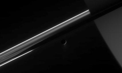 NASA's Cassini stares toward the night side of Saturn, seen here on the right, as the active icy moon Enceladus glides past.