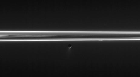 Enceladus blasts its icy spray into space in this unlit-side ring view that also features a tiny sliver of Rhea. This image was taken in visible light with NASA's Cassini spacecraft's narrow-angle camera on June 9, 2006.