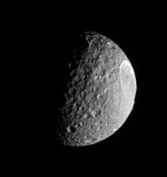 Saturn's moon Mimas plows along in its orbit, its pockmarked surface in crisp relief. The bright, steep walls of the enormous crater, Herschel gleam in the sunlight as seen by NASA's Cassini spacecraft.