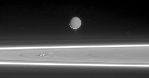 Lit by reflected light from Saturn, Enceladus appears to hover above the gleaming rings, its well-defined ice particle jets spraying a continuous hail of tiny ice grains as seen by NASA's Cassini spacecraft.