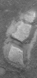 NASA's Mars Global Surveyor shows blocky remnants of a material that was once more laterally extensive on the floor of an impact crater located NW of Herschel Crater. Large ripples of windblown sediment have accumulated around and between the blocks.