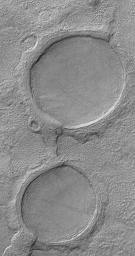 NASA's Mars Global Surveyor shows a pair of partially-buried impact craters which are being exhumed on a plain east of Hellas in the Promethei Terra region Mars.