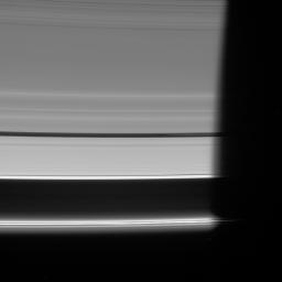 NASA's Cassini spacecraft looks down at the unlit side of the rings as Pan heads into Saturn's shadow. The moon is accompanied by faint ringlets in the Encke Gap.