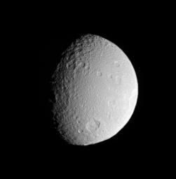 NASA's Cassini spacecraft surveys the battered surface of Saturn's icy moon Tethys. The great impact basin straddling the terminator is itself overprinted by many smaller impact sites.