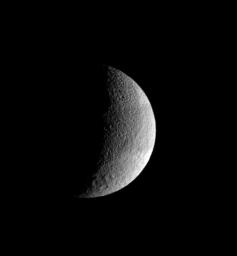 The pockmarked crescent of Tethys displays slightly darker terrain in a band at its equator. The rim of the great crater Odysseus lurks on the terminator. This image was taken in visible light with NASA's Cassini spacecraft's wide-angle camera.