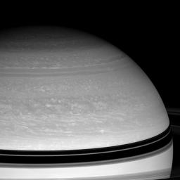 NASA's Cassini spacecraft studies the dynamics of Saturn's blustery cloud bands as spring approaches in the northern hemisphere. Janus casts its shadow onto Saturn at right, just above the curving shadow of the rings.