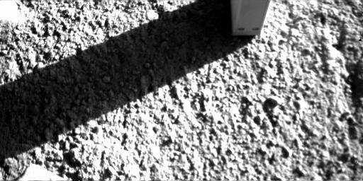 NASA's Phoenix Mars Lander inserted the four needles of its thermal and conductivity probe into Martian soil during Sept. 4, 2008 leaving an imprint visible below the probe, and a shadow showing the probe's four needles is cast on a rock to the left.