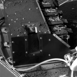 This image, taken by NASA's Phoenix Mars Lander's Surface Stereo Imager, documents the delivery of a soil sample from the 'Snow White' trench. A small pile of soil is visible on the lower edge of the second cell from the top of the deck-mounted lab.