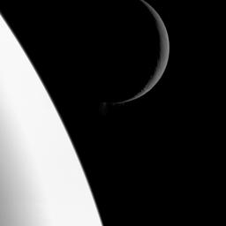 NASA's Cassini spacecraft captures this scene showing the bright crescent of Saturn's moon Enceladus at top right. The center of the image reveals plumes of water ice spew out from fractures known as 'tiger stripes' near the south pole of the moon.