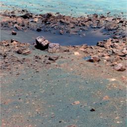 This false-color image, taken by the panoramic camera on NASA's rover Opportunity, shows the rock 'Chocolate Hills,' perched on the rim of the 10-meter (33-foot) wide 'Concepcion' crater. This rock has a thick, dark-colored coating resembling chocolate.