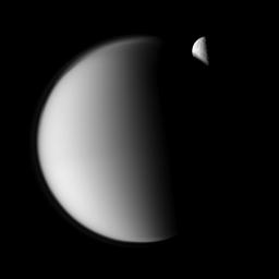 The moon Rhea moves behind Saturn's largest moon, Titan, in this 'mutual event' imaged by NASA's Cassini spacecraft. Part of Rhea's southern hemisphere is also visible here through the haze of Titan's atmosphere.
