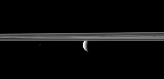 NASA's Cassini spacecraft looks past Saturn's rings and small moon Janus to spy the planet's second largest moon, Rhea where lit terrain is seen.