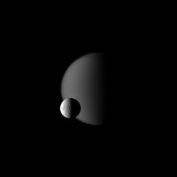 Terrain on Saturn's moon Tethys, defined with craters, is shown in front of the hazy atmosphere of the larger moon Titan in this image from NASA's Cassini spacecraft. This view looks toward the Saturn-facing sides of Titan and Tethys.