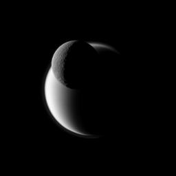A darkly defined Rhea passes before the fuzzy orb of Titan in this view from NASA's Cassini spacecraft of Saturn's two largest moons. Rhea is closer to the spacecraft in this view.