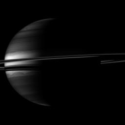 A crescent Saturn appears nestled within encircling rings in this image captured by NASA's Cassini spacecraft. Clouds swirl through the atmosphere of the planet. Prometheus appears as a speck above the rings near the middle of the image.