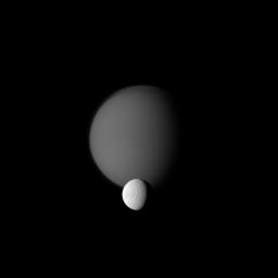 NASA's Cassini spacecraft watches a pair of Saturn's moons, showing the hazy orb of giant Titan beyond smaller Tethys. In the foreground of the image, Ithaca Chasma can be seen running roughly north-south on Tethys.