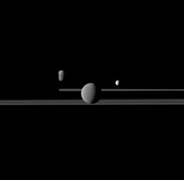NASA's Cassini spacecraft observes three of Saturn's moons set against the darkened night side of the planet. Seen here are Rhea, closest to Cassini, Enceladus to right of Rhea, and Dione, left of Rhea.