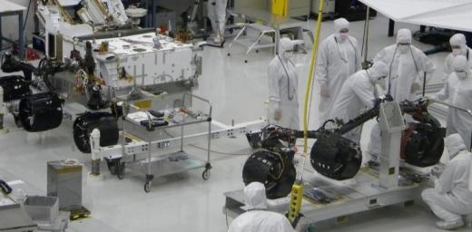 With the wheels and suspension system already installed onto one side of NASA's Mars rover Curiosity the previous day, spacecraft engineers and technicians prepare the other side's mobility subsystem for installation on June 29, 2010.