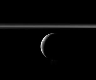 A crescent Enceladus appears with Saturn's rings in this view of the moon from NASA's Cassini spacecraft. The famed jets of water ice emanating from the south polar region of the moon are faintly visible here.